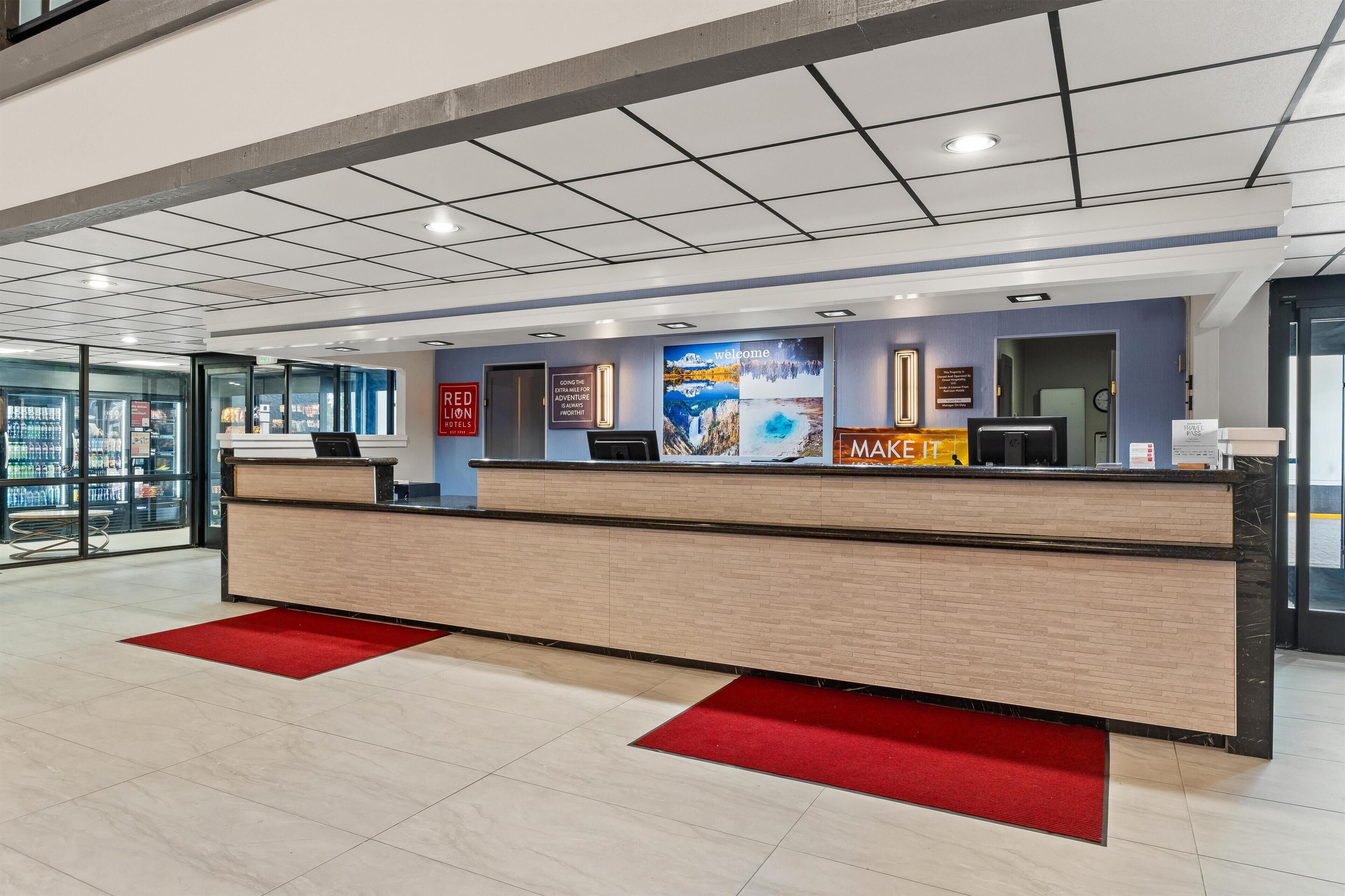 A hotel reception area with a modern design, including a reception desk, a digital screen, and a large welcome sign.