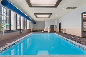 An indoor swimming pool with clear blue water, surrounded by a checkered pool edge, and a ceiling with recessed lighting.