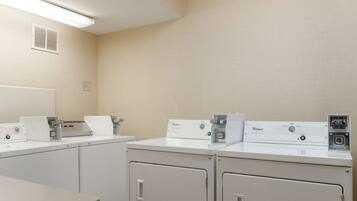 A laundry room with three Whirlpool washers and dryers, a ventilation system, and a table.