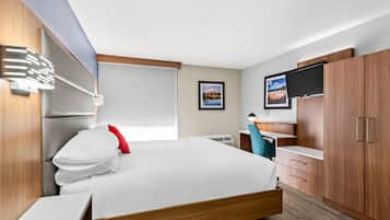 Ein modernes Hotelzimmer mit einem großen Bett, einem Holzschrank und einem Flachbildfernseher.