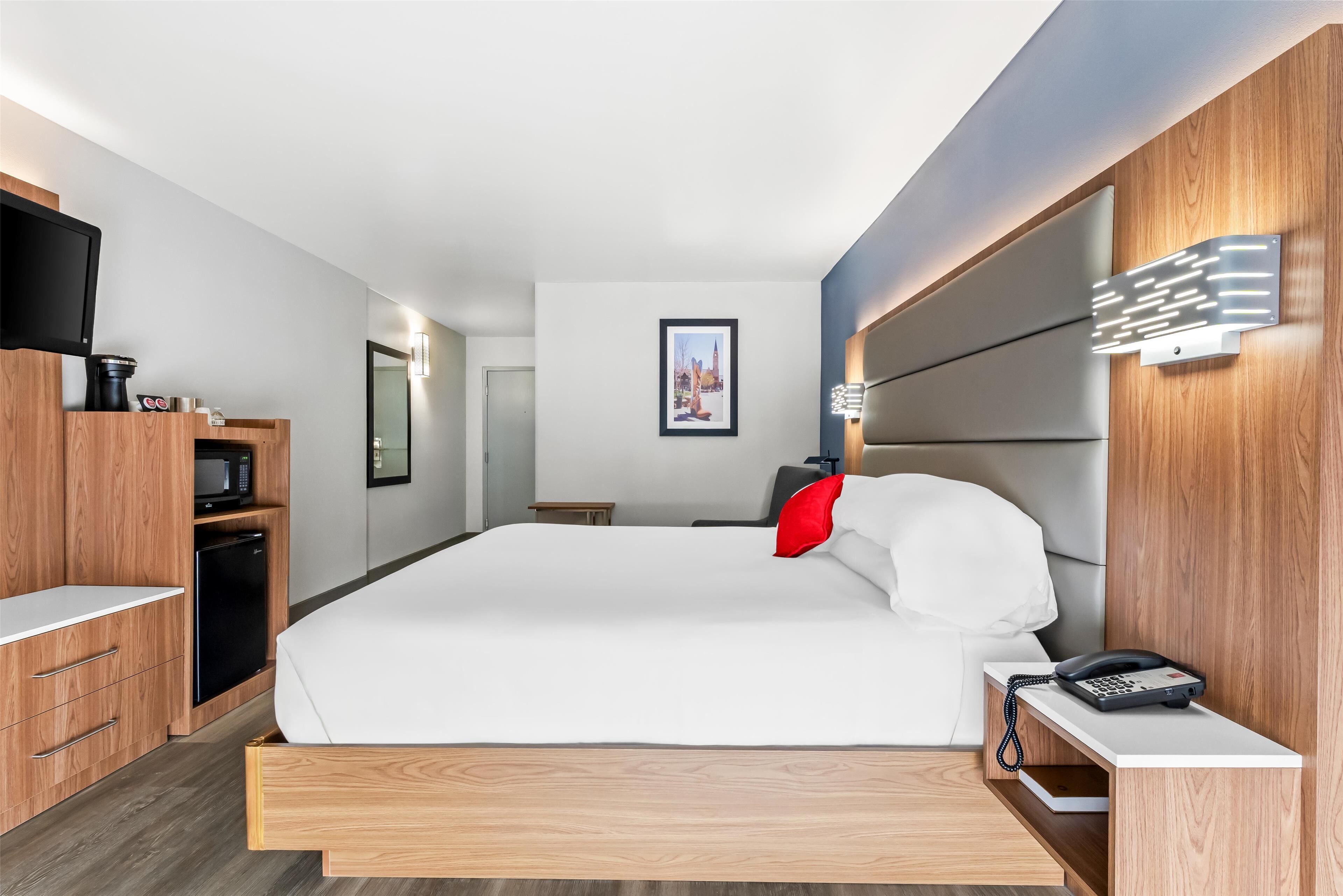 A modern hotel room with a large bed, wooden furniture, a flat-screen TV, a microwave, a refrigerator, and a bedside phone.