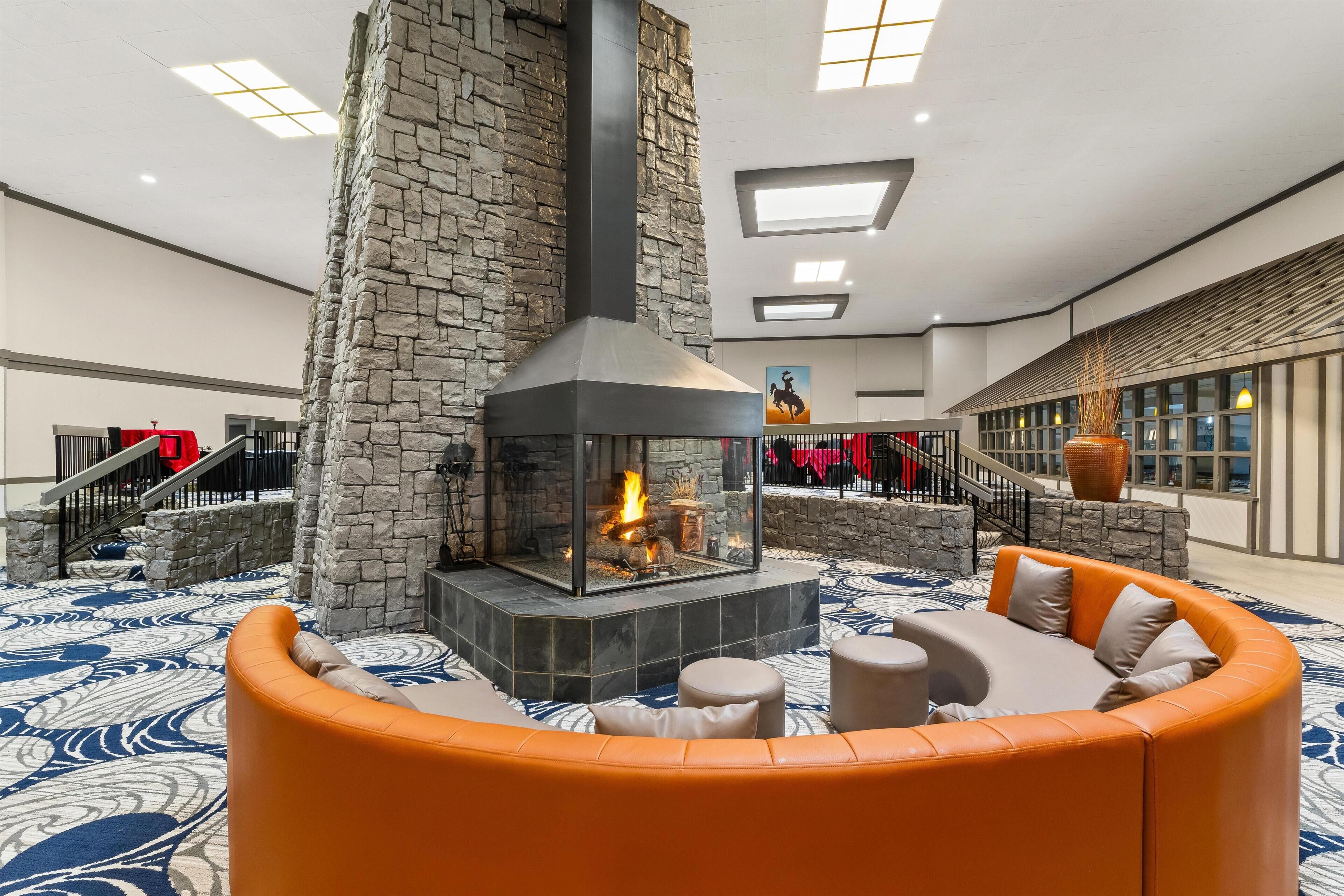 A lobby with a stone fireplace, orange seating, and a staircase.