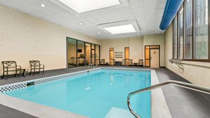 Une piscine intérieure dont le bord est orné d’un motif à carreaux, entourée de chaises et de tables, avec un plafond en lucarne et de grandes fenêtres.