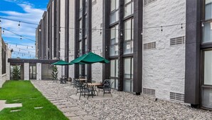 Une terrasse extérieure avec un espace salon, des guirlandes lumineuses et un parasol vert.