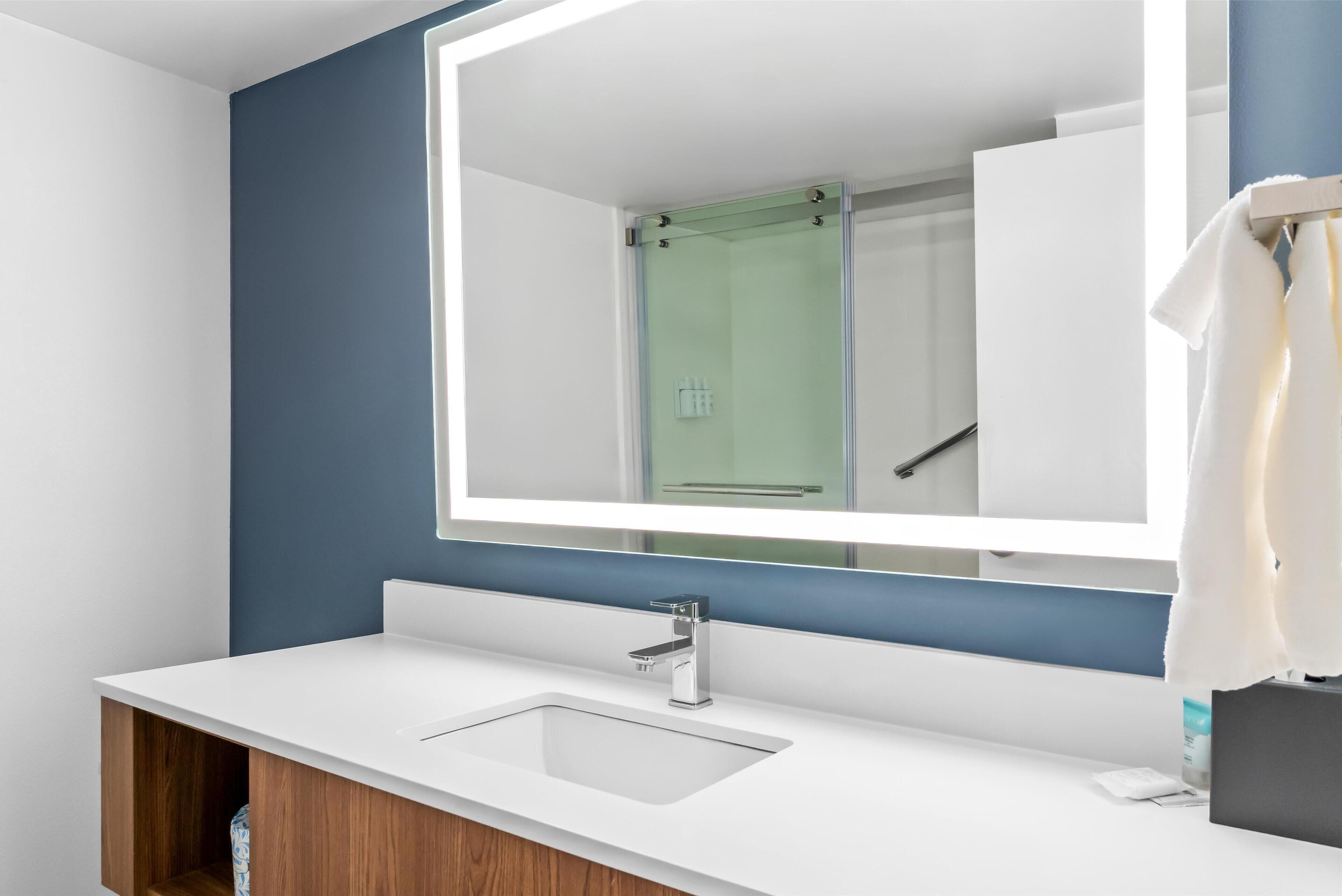 Un baño moderno con lavamanos blanco, un espejo grande y un box de ducha de vidrio.
