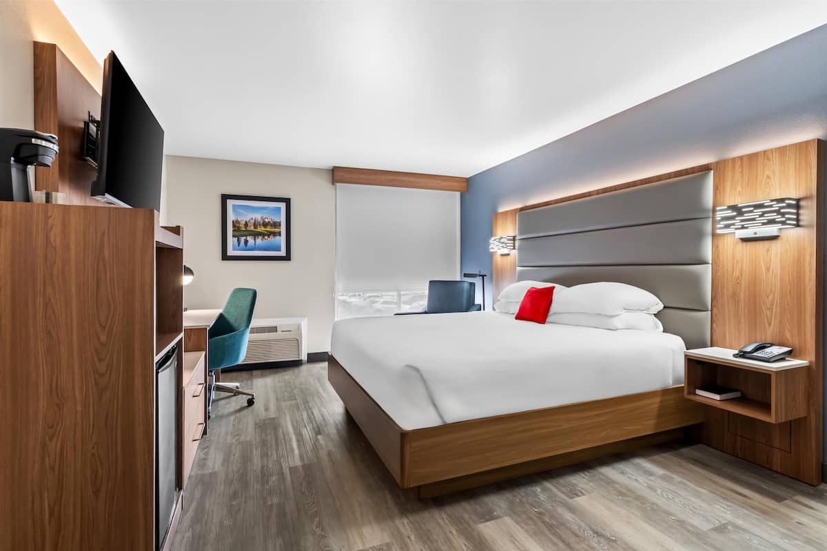 A modern hotel room with a large bed, a desk, a chair, and a TV.