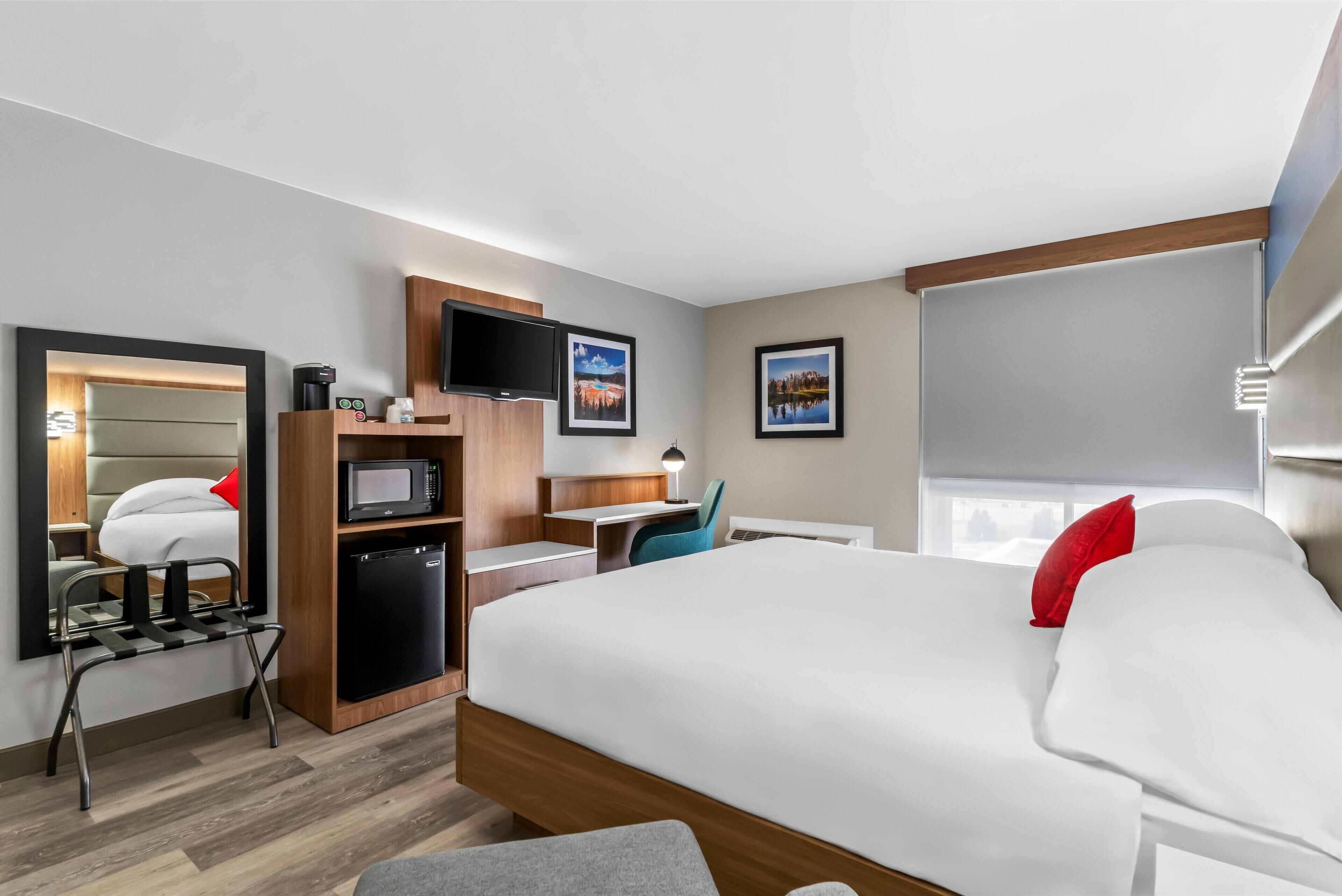 A modern hotel room with a bed, a desk, a television, and a small kitchenette.