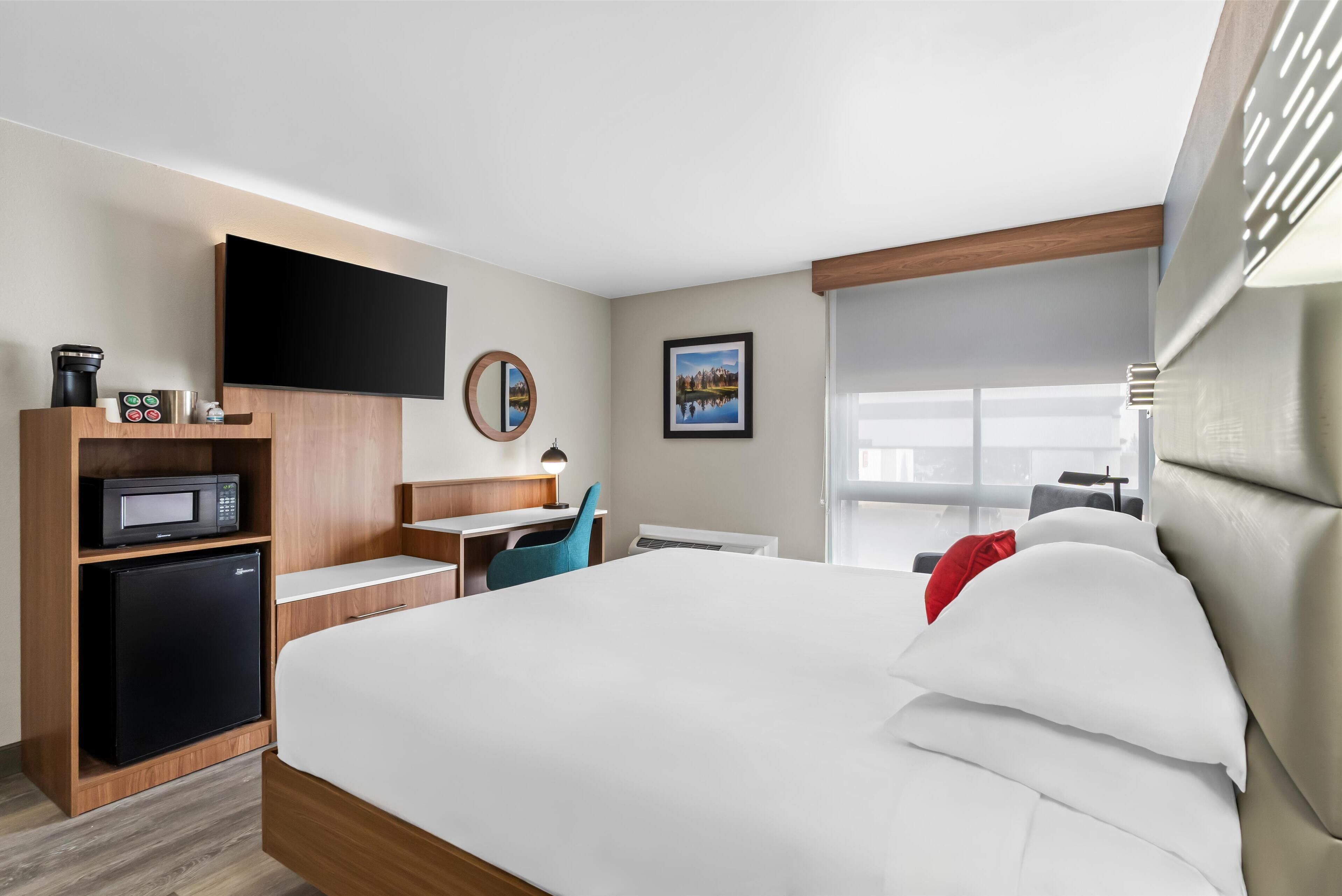 Een hotelkamer met een bed, een bureau met een computer, een magnetron en een aan de muur bevestigde televisie.