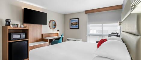 Een hotelkamer met een bed, een bureau met een computer, een magnetron en een aan de muur bevestigde televisie.