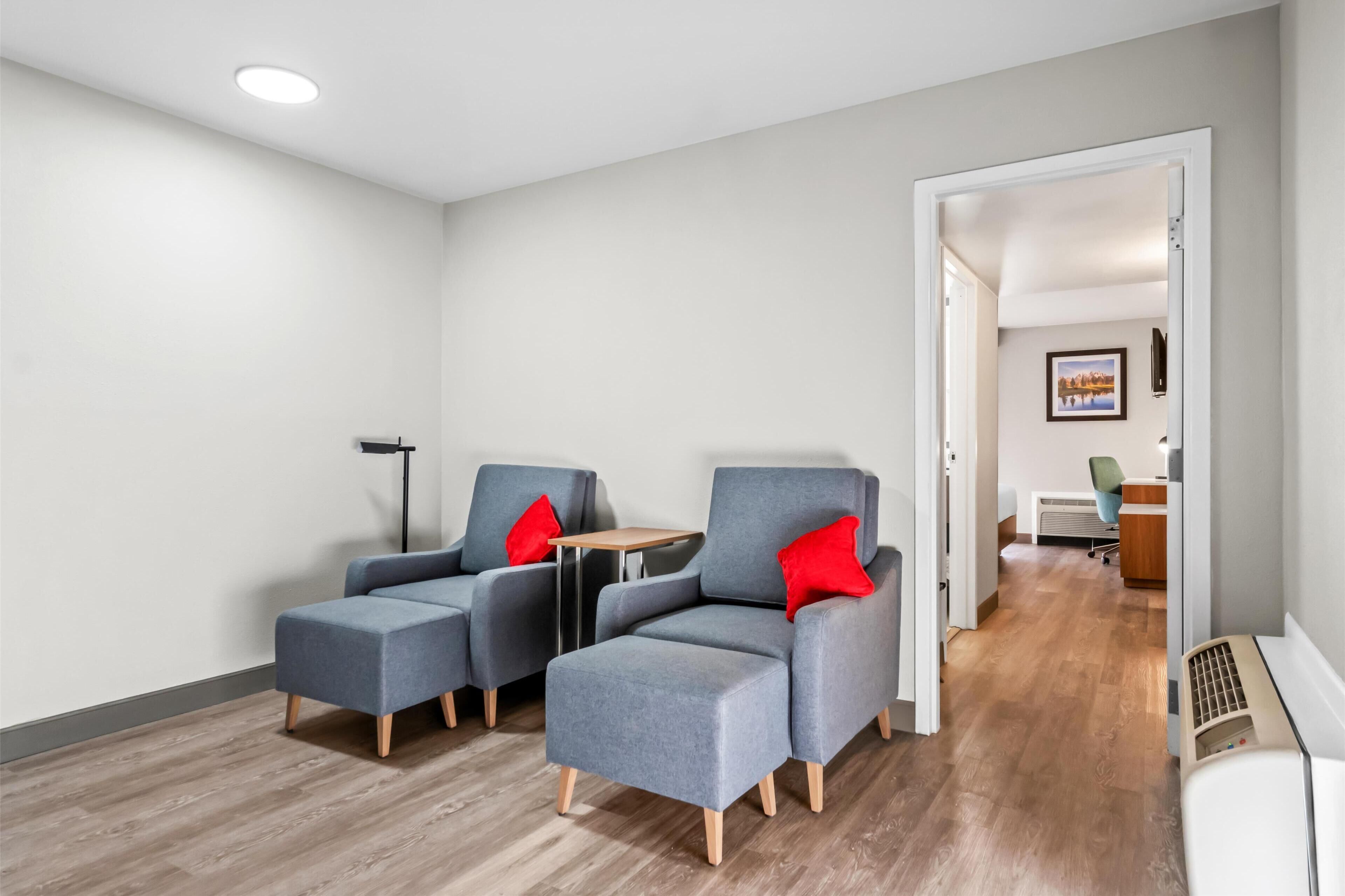 En moderne stue med grå sofaer og røde puder, et lille bord og en gulvlampe.