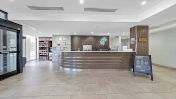 A hotel reception area with a curved reception desk, a 'Market Place' sign, and a 'Stand Clear' sign on the door.