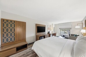 Une chambre d’hôtel avec un grand lit, un téléviseur fixé au mur, un bureau avec une chaise et une fenêtre donnant sur des immeubles.