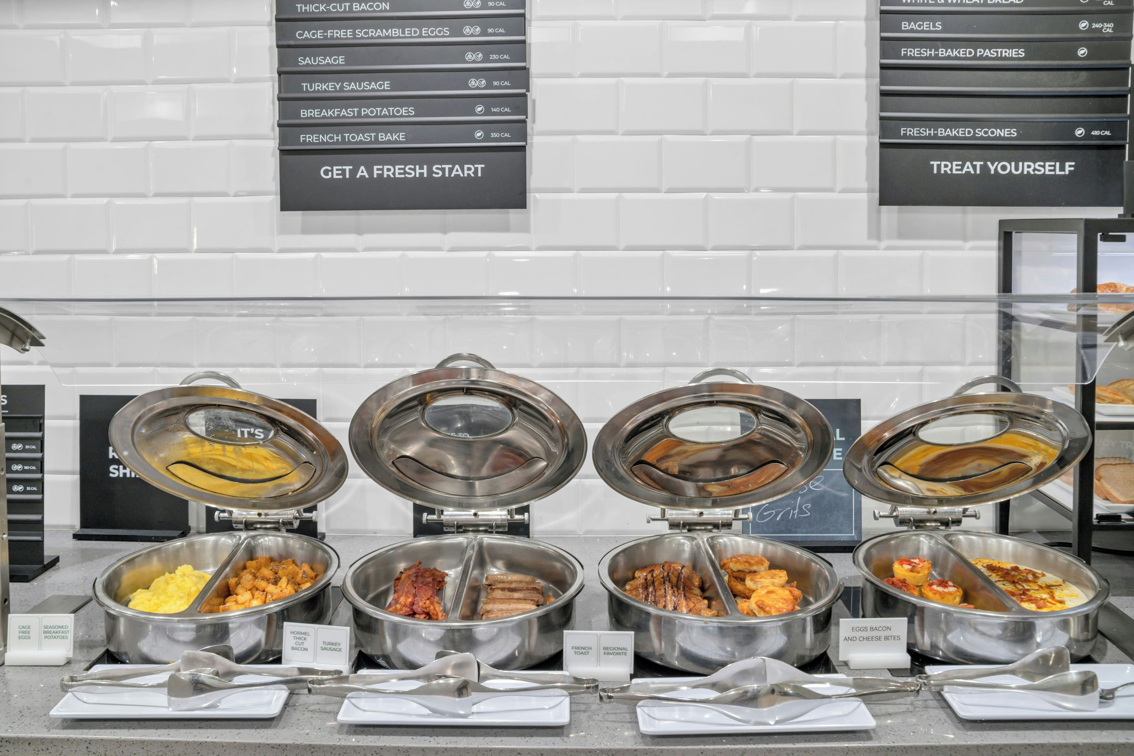 A buffet with labeled food stations including eggs, bacon, sausage, and toast.