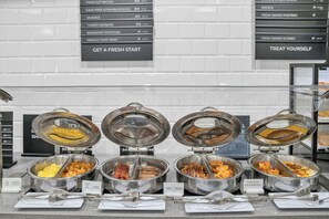 Un bufé con estaciones de comida señalizadas, que incluyen huevos, tocino, salchicha y tostadas.