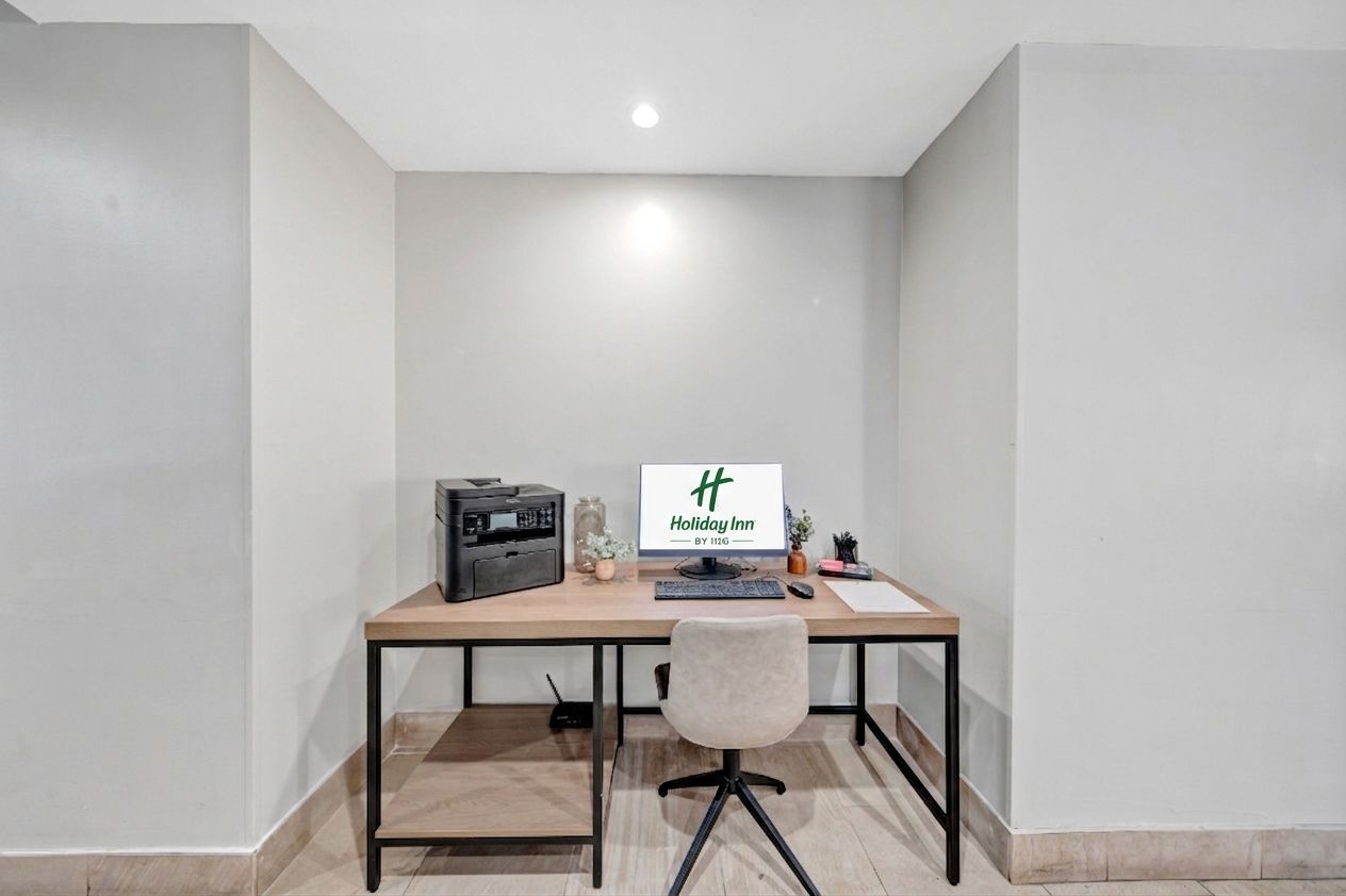 A corner office with a desk, computer, printer, and a small plant.