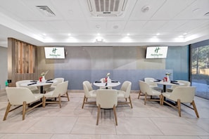 A conference room with four tables and chairs, two large screens displaying the Holiday Inn logo, and a large window with blinds. - Holiday Inn Atlanta-Northlake by IHG (Atlanta)