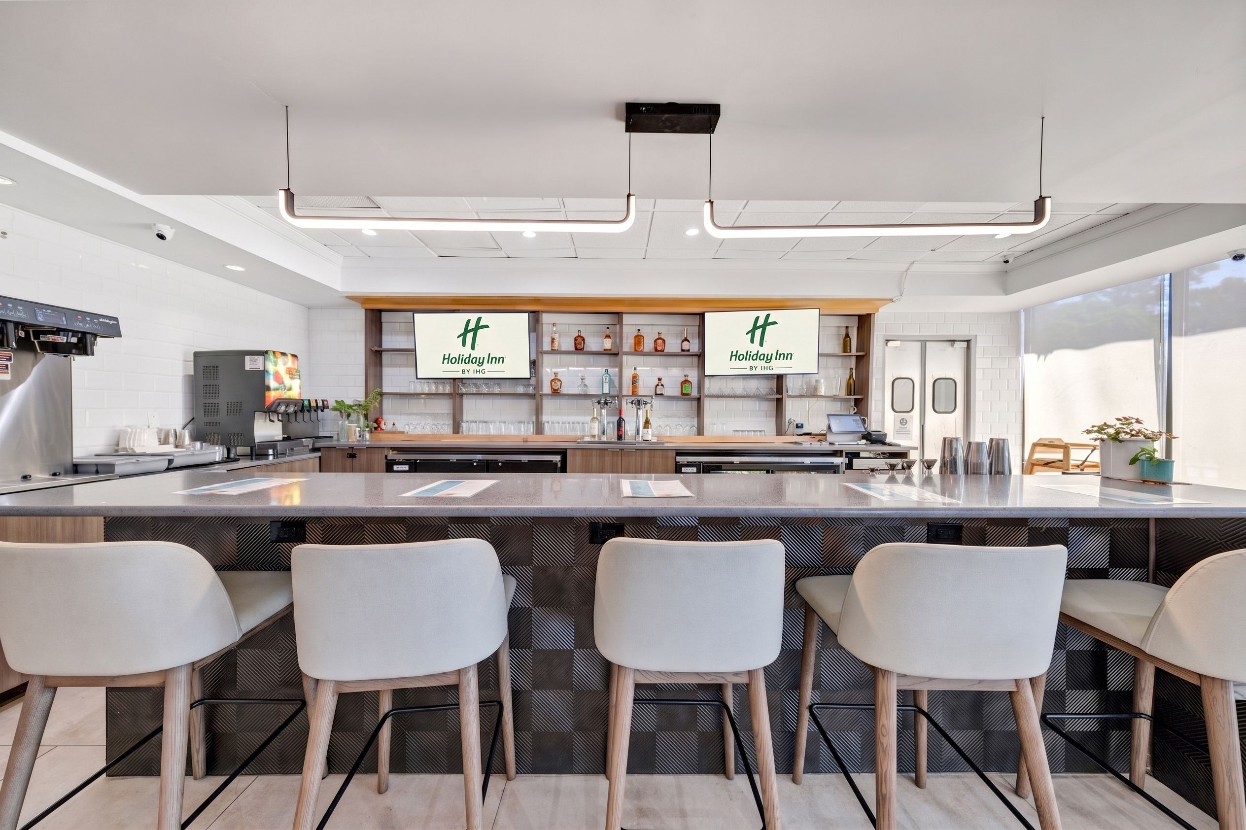 A modern kitchen with a central island, bar stools, and a display of liquor bottles.
