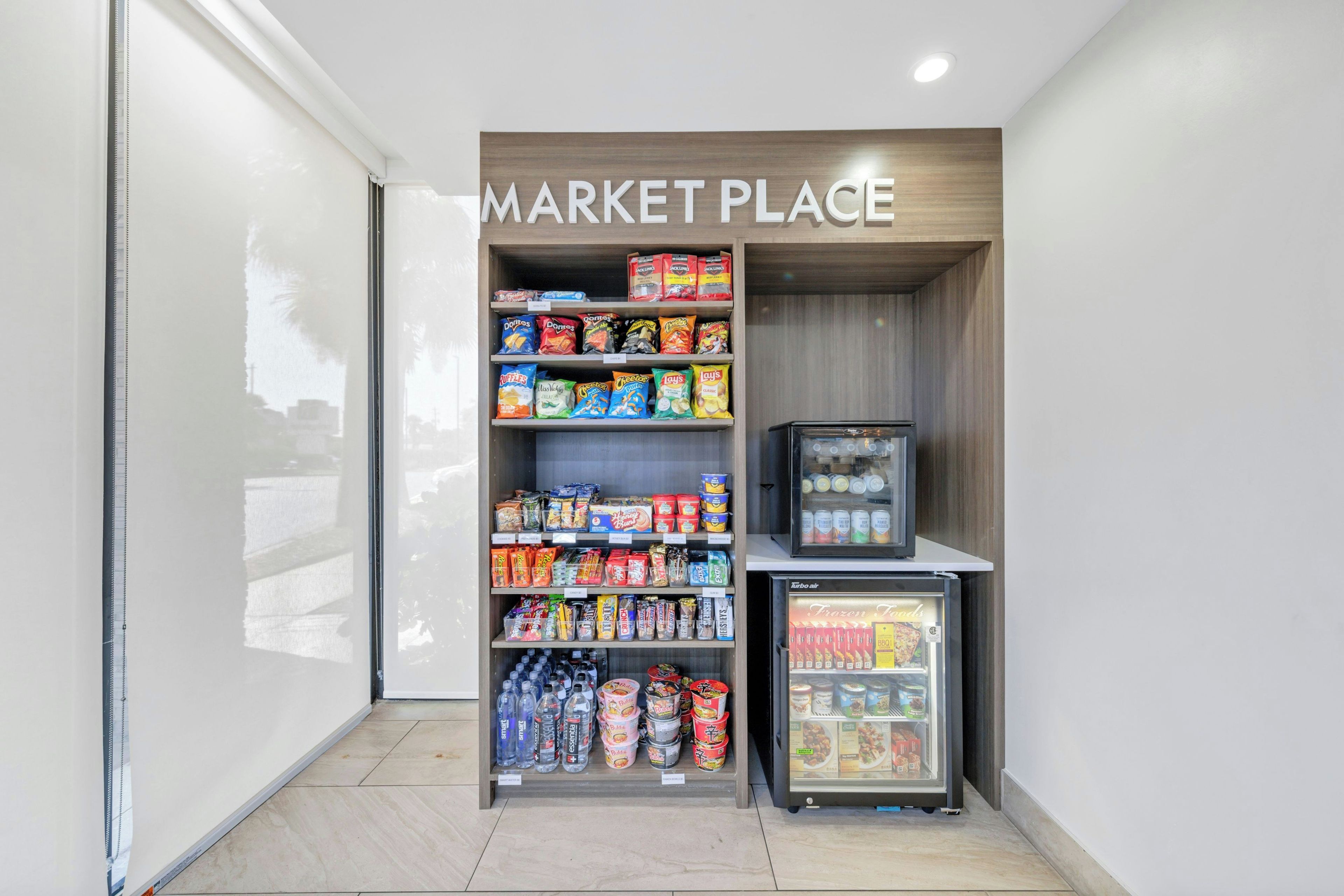 A small market area with shelves stocked with snacks, a refrigerator with frozen foods, and a vending machine.