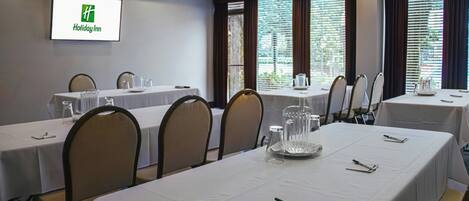 A conference room with tables set for meetings, a Holiday Inn sign on the wall, and large windows with blinds.