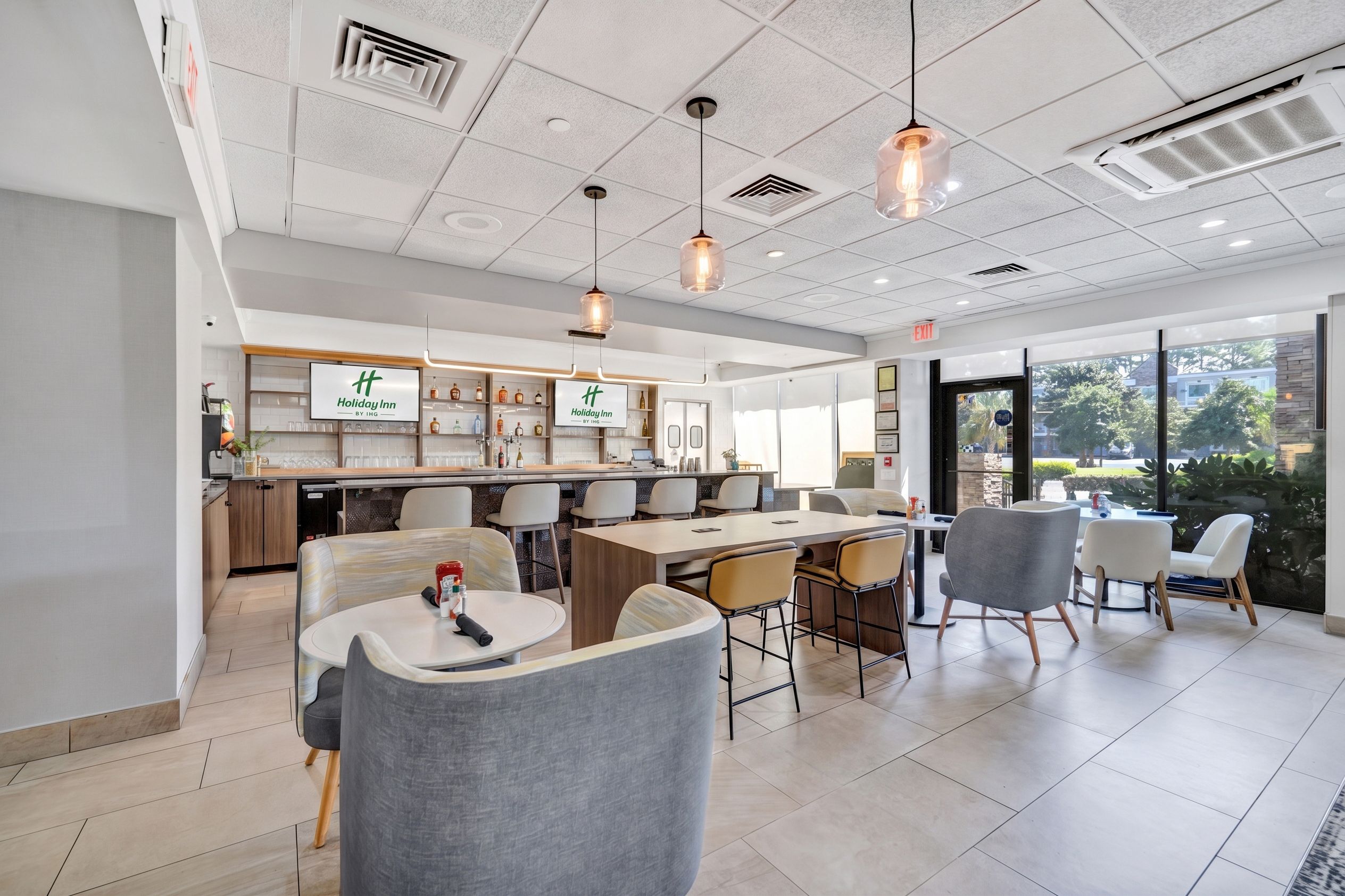 A modern hotel lobby with a reception desk, seating area, and large windows offering a view of the outdoors.
