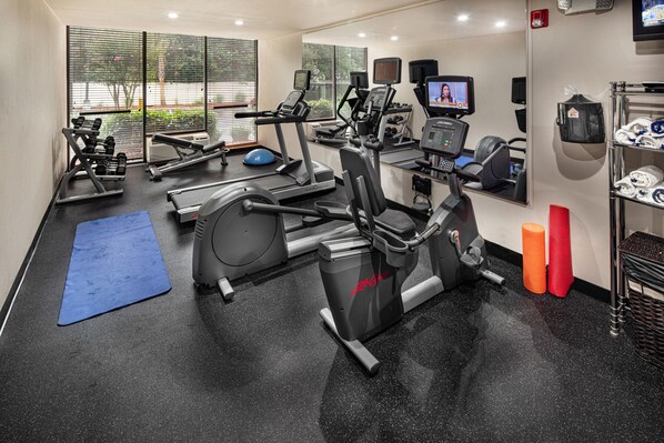 Une salle de sport équipée de machines de cardio, de poids et d’un tapis bleu.