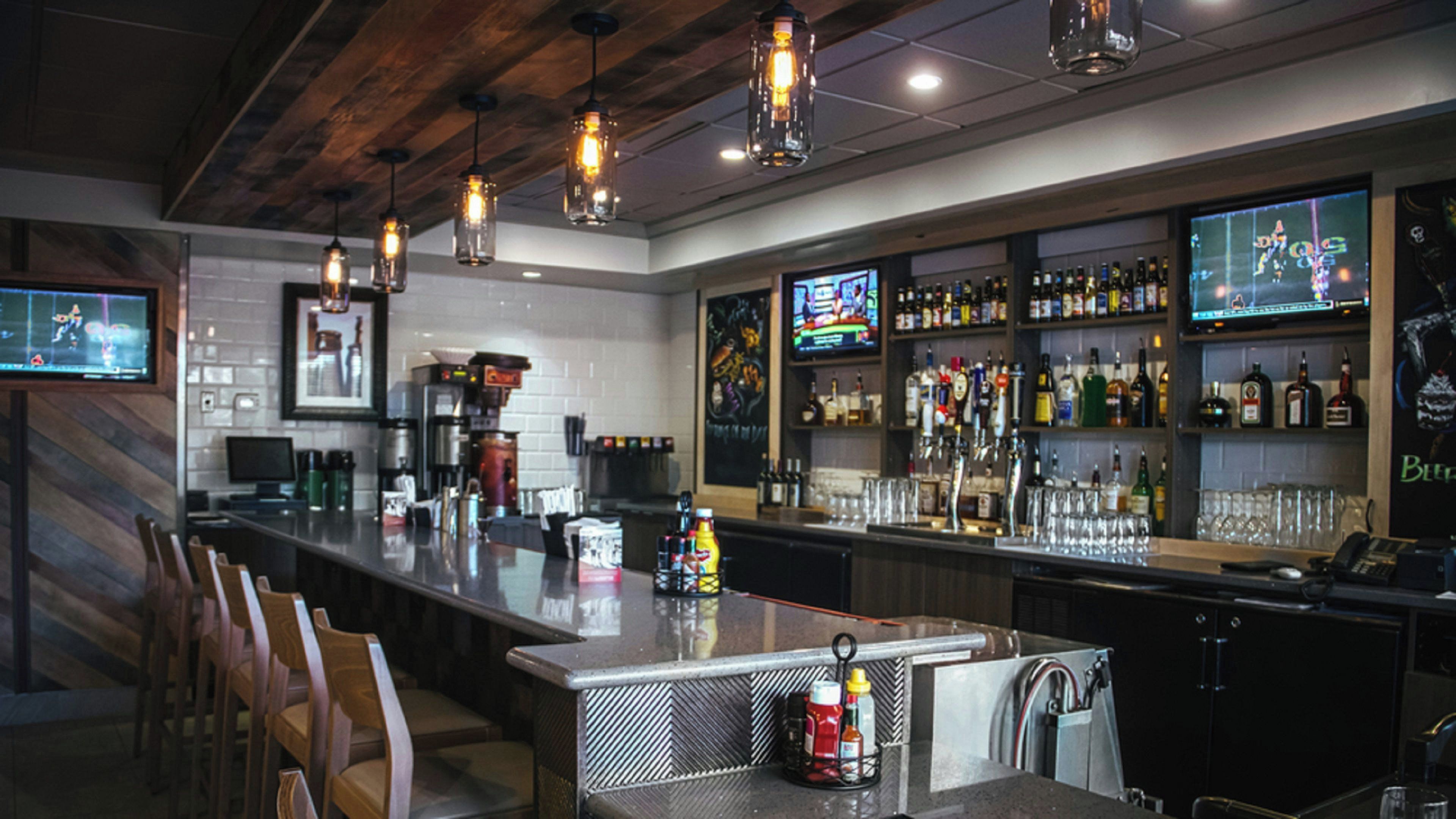 Uma área de bar com um balcão extenso, várias televisões e uma variedade de garrafas de bebidas.