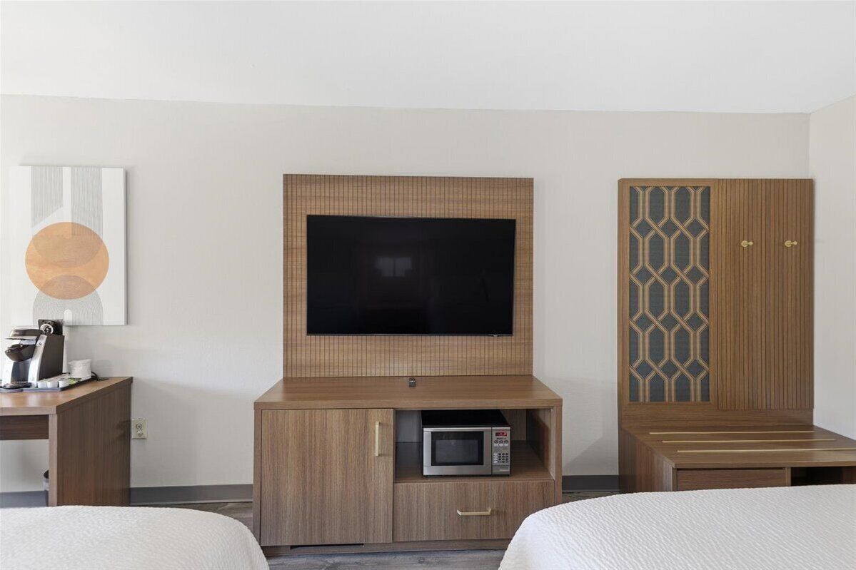 A hotel room with a TV, a microwave, a wooden cabinet, and a bed.
