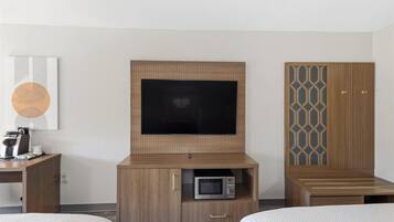 A hotel room with a TV, a microwave, a wooden cabinet, and a bed.