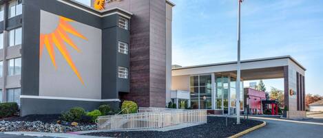 A hotel with a modern design, featuring a prominent sun logo on the facade and a flagpole with an American flag.