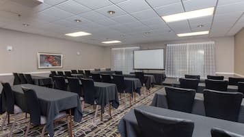 A conference room with tables and chairs, a projector screen, and a carpeted floor.