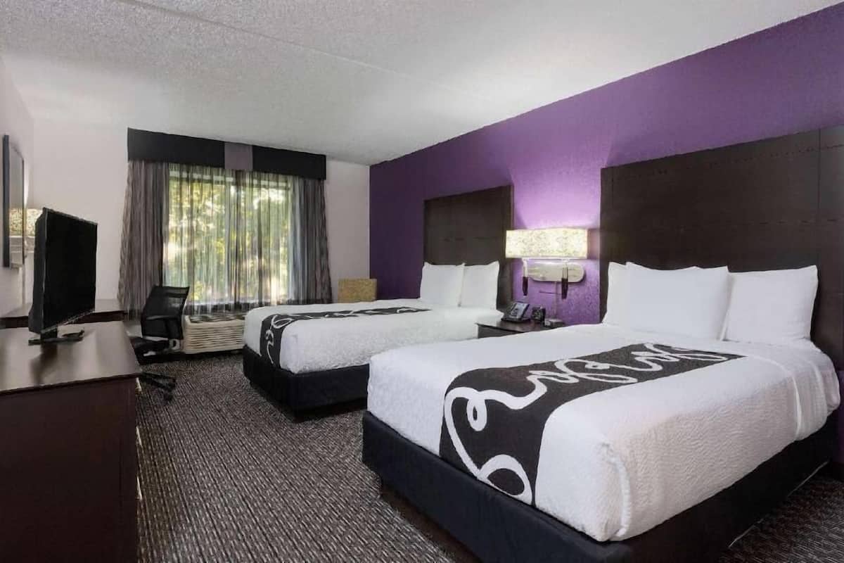 Una habitación de hotel con dos camas, un escritorio, una silla, un televisor y una ventana con cortinas.