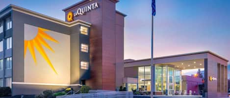 A hotel with a prominent sun logo, a flagpole, and a well-lit entrance.