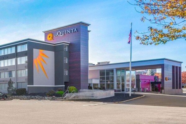 Un hotel con un llamativo letrero de 'La Quinta', un edificio moderno con ventanas grandes y un asta con la bandera estadounidense.