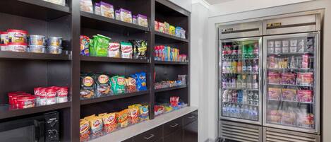 A kitchenette with shelves stocked with snacks, a microwave, and a refrigerator.