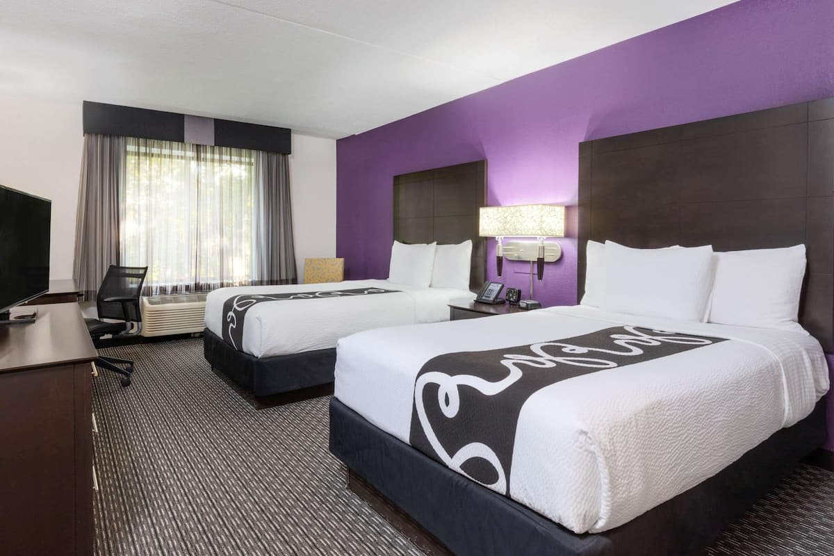 Habitación de hotel con dos camas, un escritorio, una silla, un televisor y una ventana con cortinas.