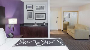 Une chambre d’hôtel comprenant un lit, un canapé, une petite kitchenette et une salle de bain visible à travers une porte ouverte.