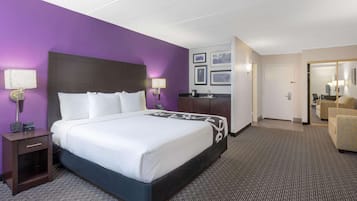 A hotel room with a large bed, a nightstand, a desk, a chair, and a bathroom visible through an open door.