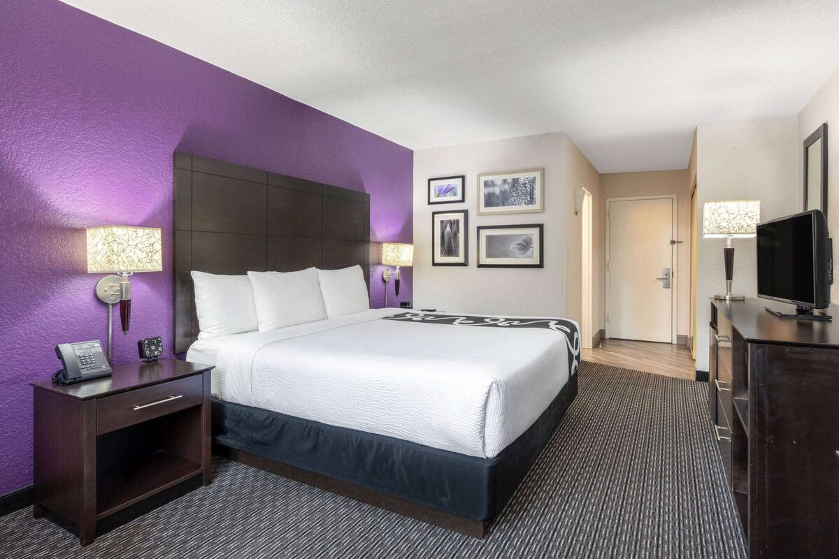 Una habitación de hotel con una cama grande, una mesita de noche con un teléfono, un televisor y cuadros enmarcados en la pared.