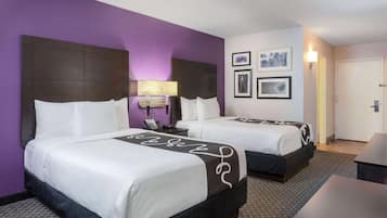 A hotel room with two beds, a desk, and a door.