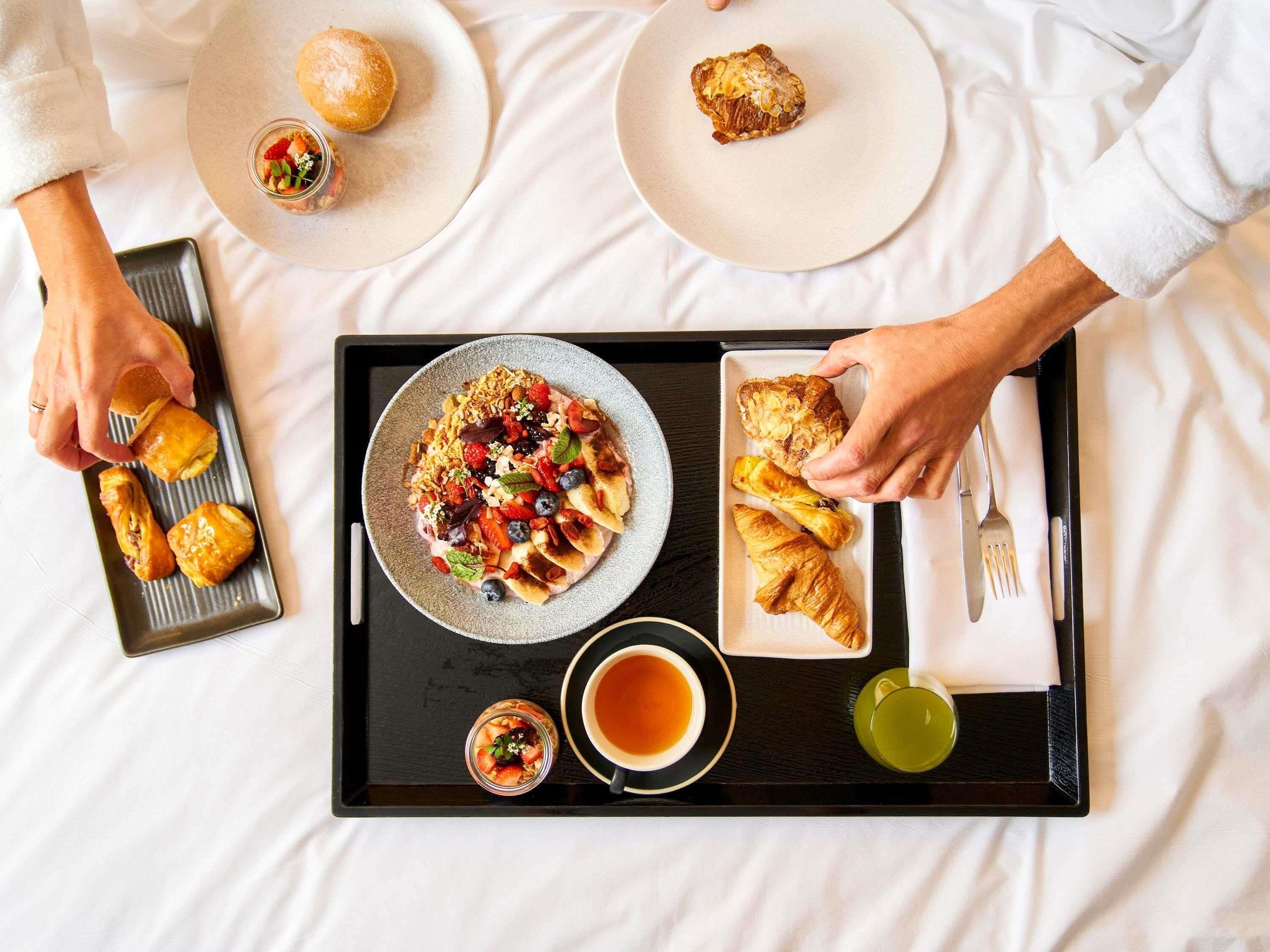 Un plateau de petit-déjeuner avec des viennoiseries, un bol de céréales et deux tasses de thé, posé sur un lit.