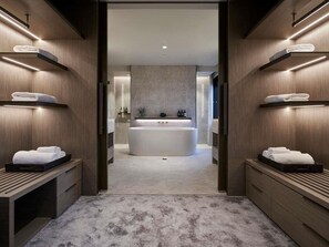 Un baño moderno con una bañera central, estanterías de madera con toallas y un suelo en tonos neutros.