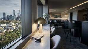 A modern hotel room with a large window offering a city view, a bar area with seating, and a minimalist decor style. - Pullman East Melbourne (East Melbourne)