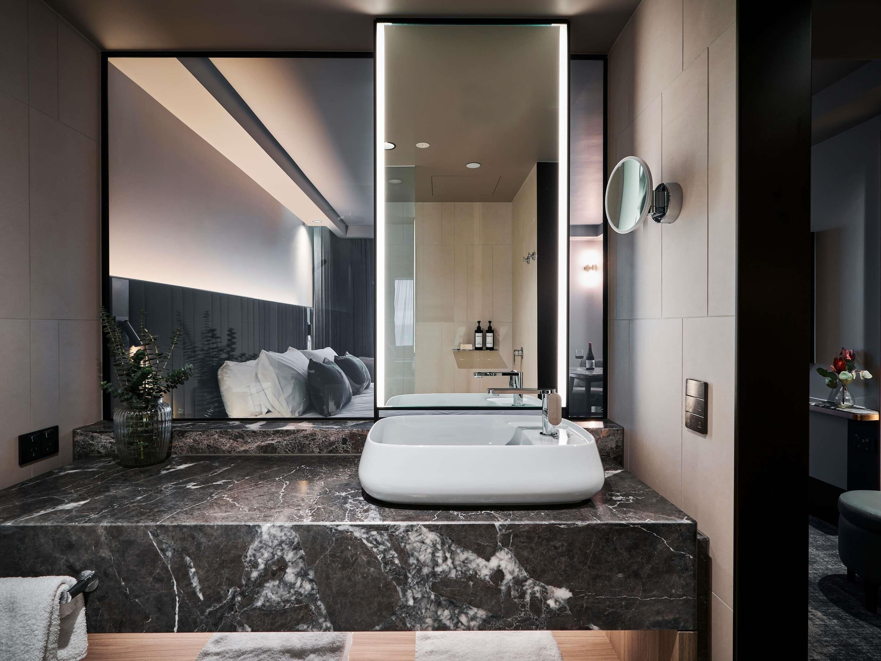 Une salle de bain moderne avec un grand miroir, un lavabo en marbre et une vue sur la chambre à coucher.