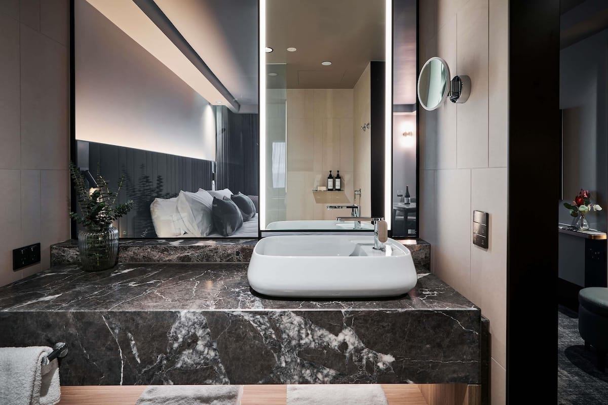 Une salle de bain moderne avec un grand miroir, un lavabo en marbre et une vue sur la chambre Ă coucher.