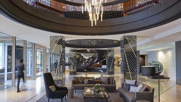 A spacious lobby with a central seating area, a spiral staircase, and a modern chandelier. - Pullman East Melbourne (East Melbourne)