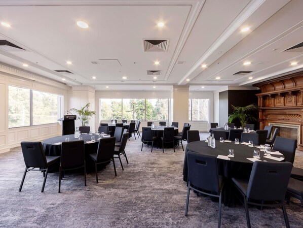 A conference room with round tables, black chairs, and a podium. - Pullman East Melbourne (East Melbourne)