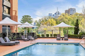 Una piscina al aire libre, sombrillas, sillones reclinables de piscina