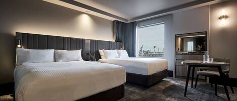 A modern hotel room with two beds, a small table, and a large window offering a city view.