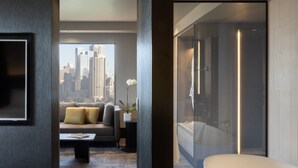 A modern hotel room with a large window, a sofa, a coffee table, and a bathtub. - Pullman East Melbourne (East Melbourne)