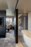 A modern hotel room with a large window, a sofa, a coffee table, and a bathtub.
